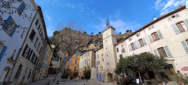 la plus belle place de cotignac sous un beau ciel bleu avec des maisons troglodytes sur les hauteurs